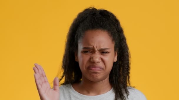 Walgelijke zwarte tiener meisje knijpen neus zwaaien hand, gele achtergrond - Video