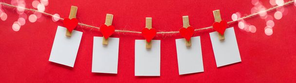 I love you - Clothes pegs with wooden hearts, bokeh lights and paper notes hang on rope isolated on red texture background banner panorama long - 写真・画像