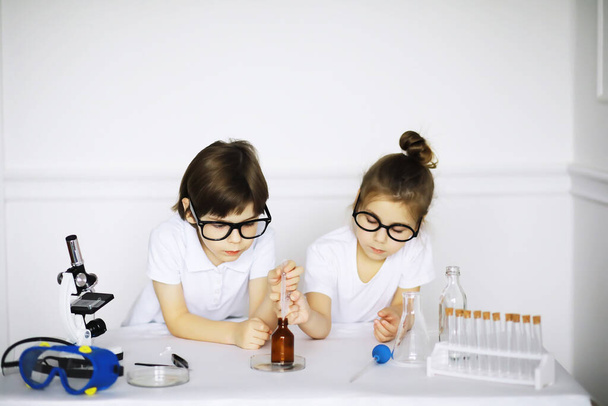 Kimya dersindeki iki tatlı çocuk beyaz arka grubunda deneyler yapıyor. - Fotoğraf, Görsel