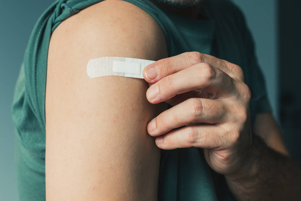 Male patient with plaster after Covid-19 vaccination and immunization procedure in hospital, selective focus - Foto, afbeelding