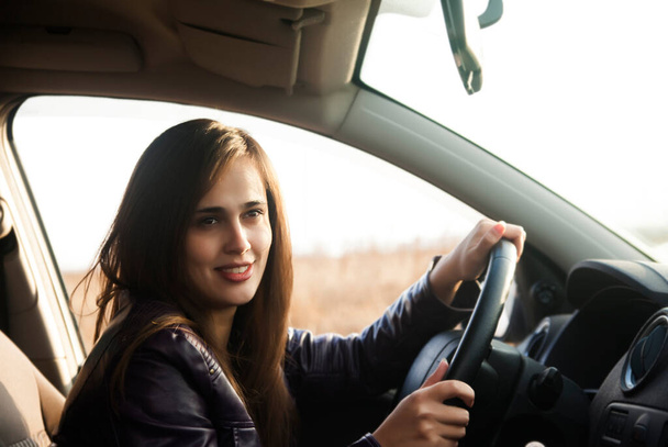 Latin kökenli genç bir kadın modern arabasının penceresinden tuhaf bir şekilde ileriye bakıyor. Başarılı, mutlu bir kızın araba sürüşünün portresi. sürüş ve araba yolculuğu  - Fotoğraf, Görsel