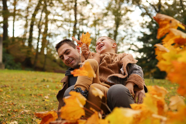 Outdoor fun in autumn. Father and son playing with autumn fallen leaves in park. - Foto, Imagen