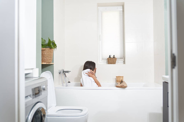 Seitenaufnahme einer Frau, die im Badezimmer sitzt. Das Mädchen wischt sich die Haare mit einem weißen Handtuch ab - Foto, Bild