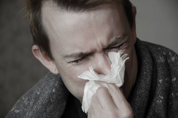 ナプキンの毛布の下で病気の白人男性。男は冷たい、疲れた病気の表情と鼻水を持っています。病期概念. - 写真・画像