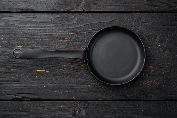 Пустая сковорода, сковородка с копировальным местом для текста или еды с копировальным местом для текста или еды, плоский вид сверху, на черном деревянном фоне стола - Фото, изображение