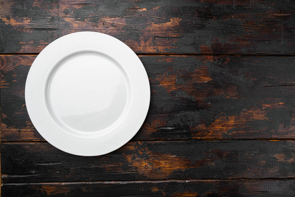 Placa blanca vacía de porcelana con espacio de copia para texto o comida con espacio de copia para texto o comida, plano de vista superior, sobre fondo de mesa de madera oscura vieja - Foto, Imagen