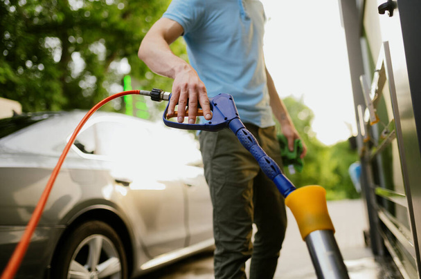 Man takes high pressure water gun, hand car wash station. Car-wash industry or business. Male person cleans his vehicle from dirt outdoors - Photo, Image