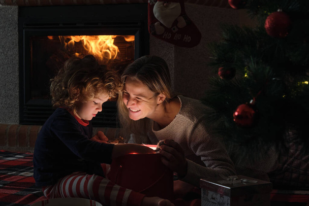 Anya és a kisfia kinyitnak egy varázslatos karácsonyi ajándékot egy karácsonyfánál. - Fotó, kép