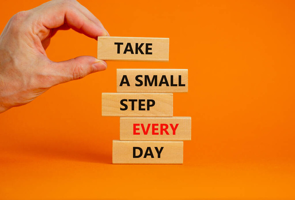 Take a small step every day symbol. Wooden blocks with words Take a small step every day. Businessman hand. Beautiful orange background, copy space. Business, step every day concept. - Foto, Bild