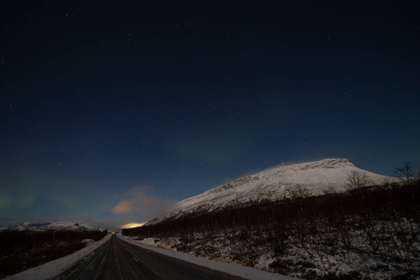 Borealis aurora barre una carretera principal en una noche sin nubes en Kilpisjarvi, Laponia, Finlandia. aurora polaris en danzas verdes a través del cielo. Magia escandinava. Montaña Saana. - Foto, imagen