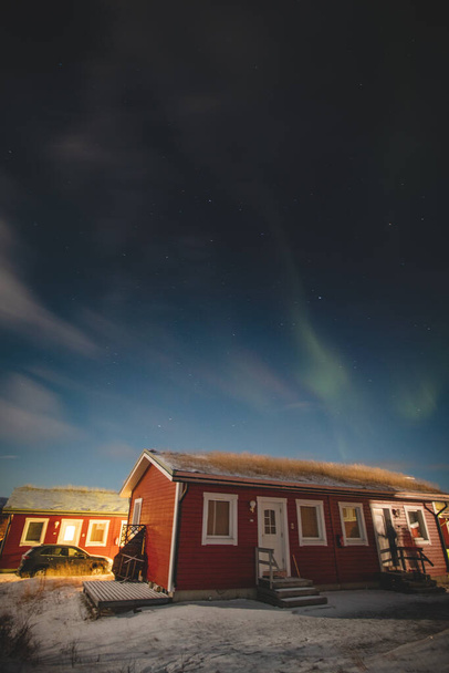 Borealis Aurora, bulutsuz bir gecede Finlandiya, Laponya, Kilpisjarvi 'de kırmızı bir kulübeyi süpürür. Aurora Polaris gökyüzünde dans ediyor. - Fotoğraf, Görsel