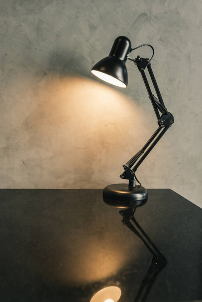 Retro black metal desk lamp or flexible table lamp light bulb decoration on the black table with cement loft-style wall interior vintage design contemporary. Modern house building concept. - Foto, afbeelding
