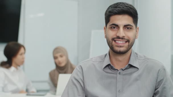 Portrait young smiling arab entrepreneur successful businessman, having triumph at meeting, built an empire, top manager with great deal of experience. His diverse subordinates working on background - Footage, Video
