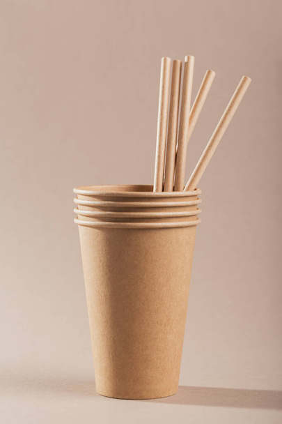 Eco-friendly disposable utensils made of craft paper on a light beige background. Paper cups and straws - Fotografie, Obrázek