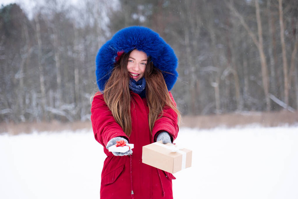 Young smiling woman in red givind gift boxes outdoors - Фото, зображення