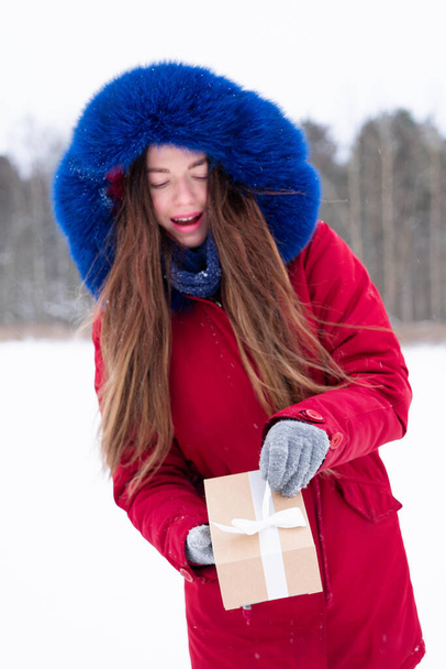 Young smiling woman in red hold gift box outdoors - 写真・画像