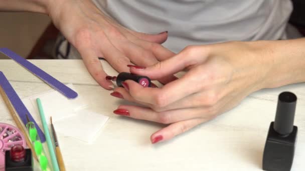 Девушка наносит бордовый лак для ногтей на ногти, самоманикюр, маникюр дома - Кадры, видео