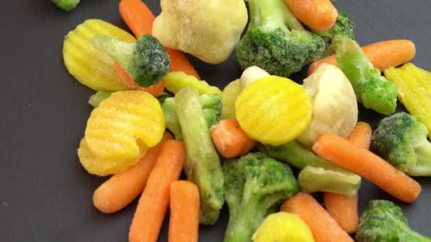 Aliments sains ou diététiques pour végétariens et végétaliens, légumes frais congelés tournant sur fond noir, chou-fleur congelé, brocoli et bébés carottes - Séquence, vidéo