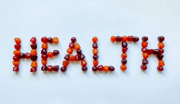Un grupo de gomitas multivitamínicas rojas, naranjas y púrpuras dispuestas en forma de la palabra salud - Foto, Imagen
