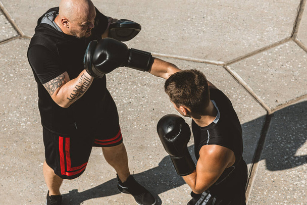 Two men exercising and fighting in outside. Boxer in gloves is training with a coach - 写真・画像