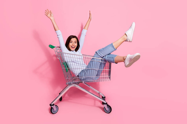 Photo of adorable funky young lady dressed white jumper smiling having fun shopping trolley isolated pink color background - Foto, Imagen