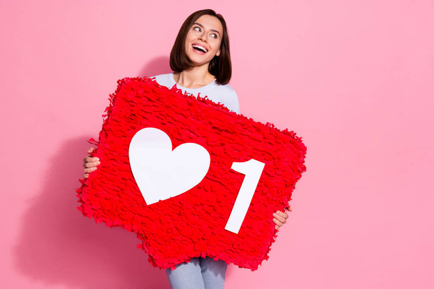 Photo of dreamy charming young lady dressed white jumper holding huge like sign pinata looking empty space isolated pink color background - Zdjęcie, obraz