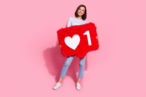 Photo of shiny adorable young woman wear white sweater walking holding big like heart sign smiling isolated pink color background - Фото, изображение