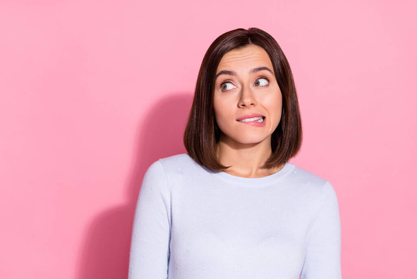Photo of pretty doubtful young lady dressed white jumper biting lip looking empty space isolated pink color background - Foto, Imagem
