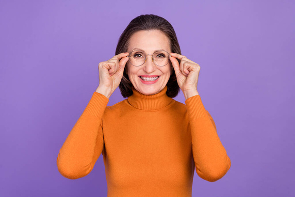 Photo of charming cute lady pensioner dressed orange turtleneck arms glasses smiling isolated purple color background - Foto, immagini