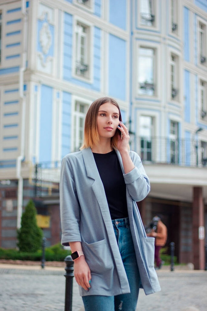 Business woman talking on the phone outdoors. Portrait of beautiful smiling girl in fashionable office clothes. Remote work - Zdjęcie, obraz