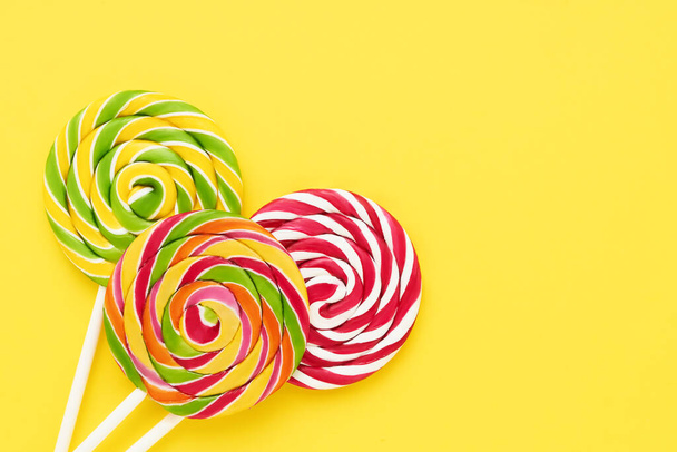 Three colorful lollipops on a white stick on a bright yellow background. Top view, copy space - Fotoğraf, Görsel