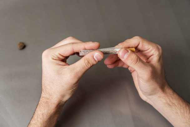 Homem adulto mãos rolando tabaco misto com filtro na mesa cinza - Foto, Imagem