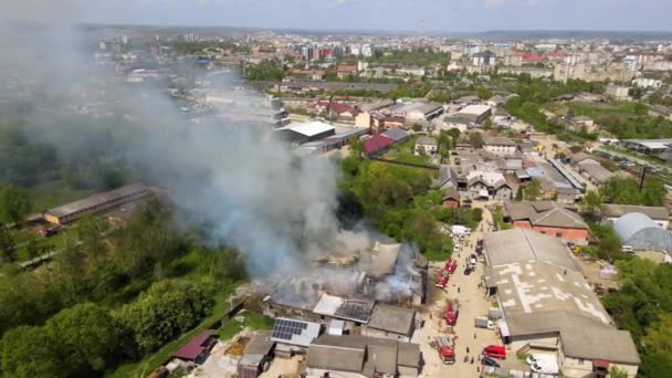 Aerial view of firefighters extinguishing ruined building on fire with collapsed roof and rising dark smoke - Footage, Video