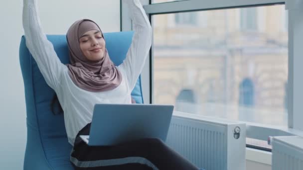 Ontspannen mooie moslim Arabische zakenvrouw werknemer zit in comfortabele fauteuil mediteren, positieve kalme Arabische vrouw ontspannen vasthouden hand achter hoofd droom rust van computer stretch gevoel gemoedsrust - Video