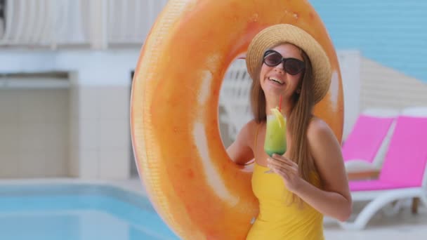 Bella donna bionda caucasica esile abbronzata in occhiali da sole beve succo di frutta in piscina in hotel spa. Ragazza europea in costume da bagno godere di vacanza di lusso con cocktail, porta anello gonfiabile salvagente - Filmati, video