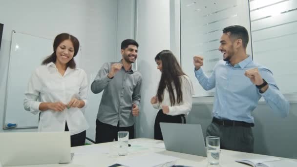 Nadšení motivovaní úspěšní kolegové z řad různorodosti, radující se a oslavující týmový úspěch v úřadu. Šťastní zaměstnanci tančí, dělají vítězná gesta, smějí se a baví se spolu. Jednota, koncepce týmové práce - Záběry, video