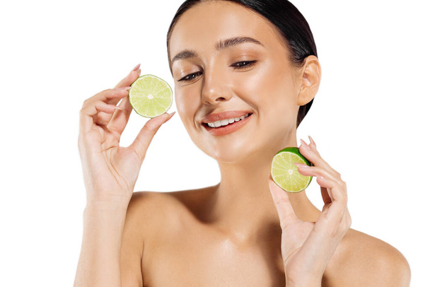 Healthy beautiful young woman, with clean skin, holding lime halves near the face, healthy eating concept, woman posing with citrus fruits in front of the camera, isolated on white background - Valokuva, kuva