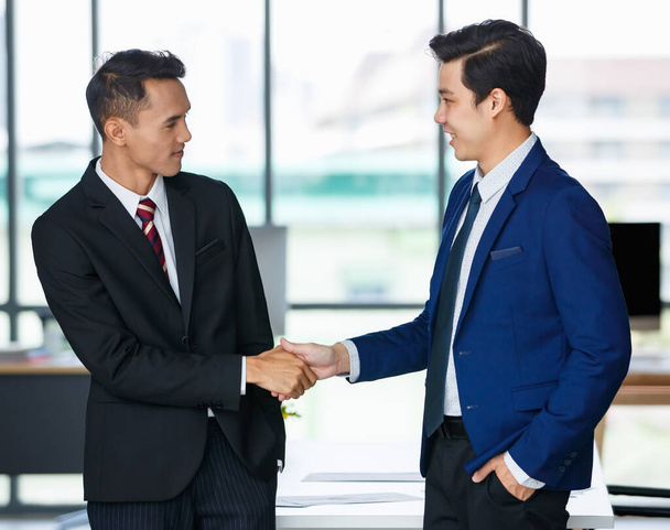 Encantado Asiático empresários do sexo masculino em ternos apertando as mãos e olhando uns para os outros após negócio bem sucedido no local de trabalho - Foto, Imagem