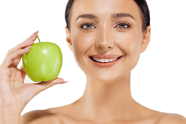 Портрет красивой молодой женщины с идеальной улыбкой, улыбающейся женщине со здоровыми зубами, держащей зеленое яблоко, на изолированном белом фоне - Фото, изображение
