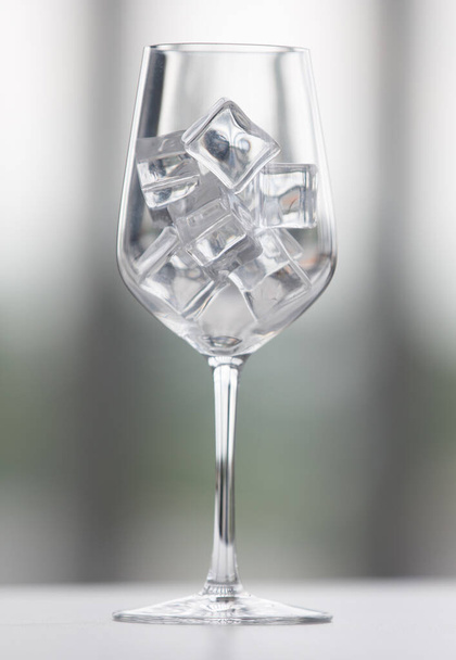 Glass goblets with ice cubes placed on table on blurred background of window - Foto, Imagen