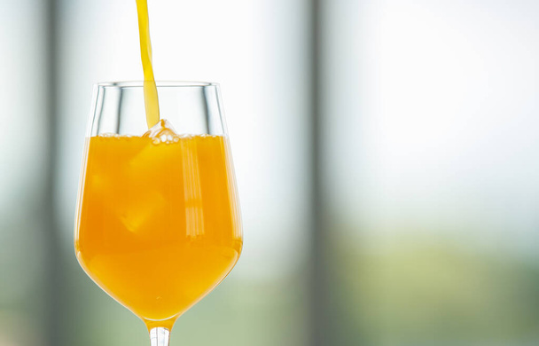 Goteo de jugo de naranja fresco vertiendo en el vaso con cubitos de hielo sobre fondo borroso - Foto, imagen