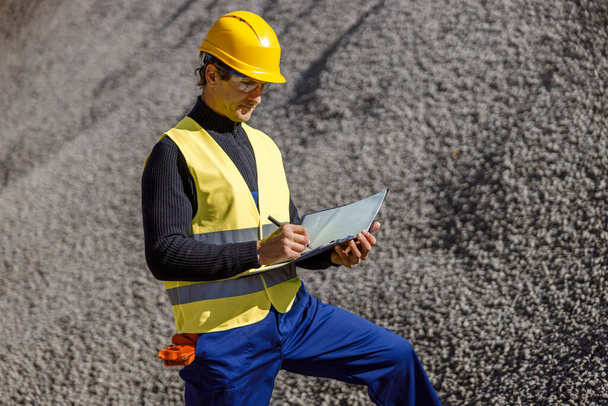Male worker writing documents outdoors at cement factory - Photo, Image