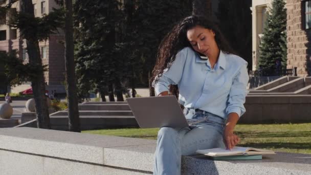 Monitoiminen nuori tyttö liiketoiminnan nainen freelancer tutkimus työskentelee kannettavan puhuvan matkapuhelimen lukeminen kirja tekee muistiinpanoja puhelun kirjoittaa istuu kadulla toimistossa college rakennus tausta - Materiaali, video