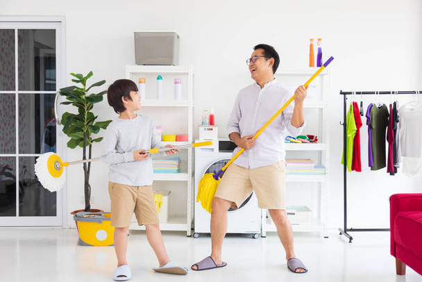 Aziatische vader en zoon helpen elkaar om de vloer te reinigen met behulp van dweil en emmer voor dagelijkse routine klusjes en huishoudelijke concept - Foto, afbeelding