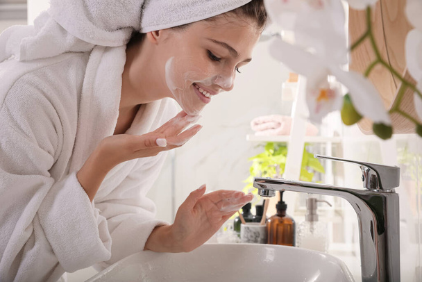 Beautiful teenage girl applying cleansing foam onto face in bathroom. Skin care cosmetic - 写真・画像