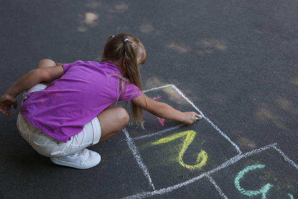 Little girl drawing hopscotch with chalk on asphalt outdoors. Happy childhood - Фото, изображение