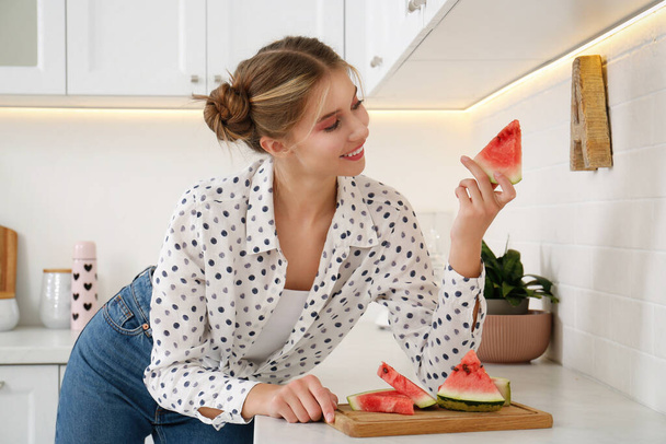 Beautiful teenage girl with slice of watermelon near countertop in kitchen - Foto, immagini