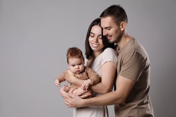 Happy family. Couple with their cute baby on grey background, space for text - Zdjęcie, obraz