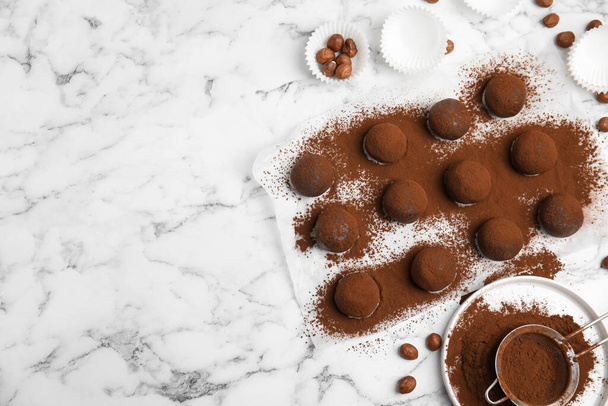 Delicious chocolate truffles with cocoa powder and hazelnuts on white marble table, flat lay. Space for text - Φωτογραφία, εικόνα