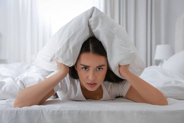 Unhappy young woman covering ears with pillow in bed at home. Noisy neighbours - Foto, afbeelding